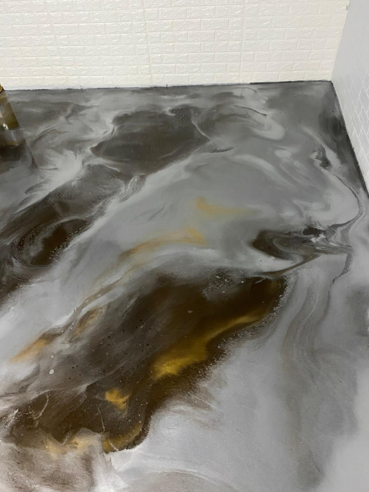 Silbergrauer Boden mit goldenen und dunklen Akzenten vor einer weißen Wand